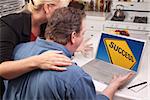 Couple In Kitchen Using Laptop with Yellow Success Road Sign on the Screen.