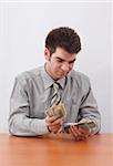 Young businessman counting US paper currency with sitting at the table.