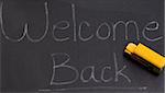 A black board with the words welcome back, and also a small toy school bus