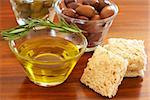 Two jars of green and black olives with stick of rosemary, olive oil and slices of bread on wooden table background