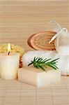 Natural skincare cleansing products lit by a candle and set against a bamboo background.