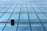 Smooth contemporary blue glass panels wall reflecting the sky. One facade system cube light in front.