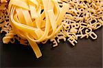 Tagliatelle and alphabet soup pasta. Italian food on black background.