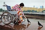 Woman in wheelchair feeds pigeons in street cities