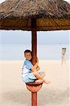 Little boy under a beach umbrella near the sea summer dress