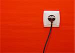 Electric outlet on red wall with cable connected