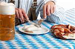 close-up of Bavarian man having lunch at Oktoberfest with beer stein (Mass), Sausage (Weisswurst) and Pretzel (Brezn)