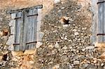 Abandoned house exterior. Stone wall and weathered window shutter detail.