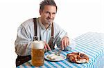 Bavarian Guy is sitting at table and having a typical Oktoberfest meal with pretze (Brezn), veil sausage (Weisswurst), beer at beer stein (Mass). Isolated on white background.