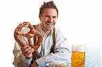 Bavarian Man is sitting on bench and holding in his hand an Oktoberfest Pretzel. Beside him is a full Beer Stein (Mass).