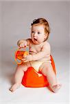 Baby on orange potty with orange bottle in hands