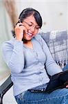 Portrait of young Asian woman talking on the phone while examining her laptop