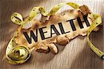 Measuring wealth concept using burnt paper with word wealth printed on it and golden rocks surrounded by measuring tape