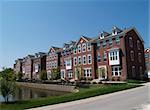 A row of brick condos or townhouses with bay windows beside a street.
