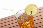 A glass of ice tea with lemon slice and straw on wooden background. Shallow depth of field