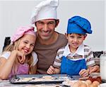 Happy father and children baking cookies together in the kitchen