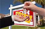 Agent Handing Over the Key to a New Home with Real Estate Sign and House in the Background.