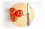 Three tomatos and stainless knife on wood plate