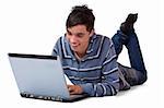 Young teenager is lying on floor and surfing on his laptop
