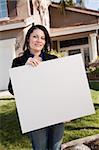 Happy Attractive Hispanic Woman Holding Blank Sign in Front of House.