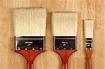 Three Different Sized New Paint Brushes on a Wood Surface.
