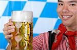 Asian Boy is holding a full Oktoberfest beer stein and smiles happy in camera. Isolated on white.