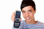 Young handsome teeanger smiles happy and holds mobile phone into camera. Isolated on white.