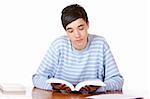 Young male student sitting on desk reading a study book and smiles happy into camera. Isolated on white.