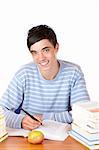 Young student is sitting on desk with study books and learns for his exams. He smiles happy into camera. Isolated on white.