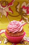 Fresh vanilla cupcake in pink cup with strawberry icing on decorative background