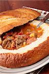 Goulash soup with beef, potato and meat sausage, served in a bread bowl
