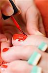 Closeup of a womans toes being painted with red nail polish.