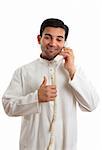 Happy ethnic mixed race businessman on telephone with thumbs up approval, success hand sign.   He is wearing a traditional robe, thobe, kurta with buttons of red burmese rubies set in silver.