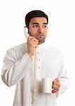 Unsure businessman from middle east, India or south east asia.  He is wearing a traditional robe, is on the telephone and  looks worried or anxious while looking sideways - white background