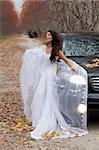 Young woman in a wedding dress standing near the jeep in an autumn forest
