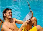 Attractive man uses his laptop while tanning poolside