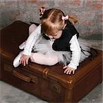 Tiny travelling ballerina sitting on a suitcase wearing a leather undercoat over her tutu