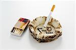 Cigarette in skull ashtray, with 'See You Later' motif and matches on a tabletop