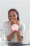 Afro-american businesswoman saving money in a piggybank at her desk