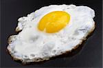 Fried egg over black textured plate background