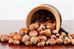 Ceramic mug with spilled different-sized hazelnuts on a wooden table