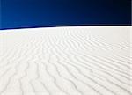 White sand dune with wind patterns and bright blue sky