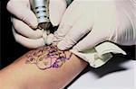 A tattoo artist applying his craft onto the hand of a female