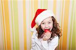 beautiful little girl bites a red heart wearing santa claus red hat