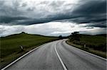 Road between fields under a cloudly sky
