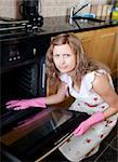 Annoyed woman cleaning the oven in the kitchen