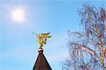 Golden figure of the Archangel with the pipe in the background of sky and tree