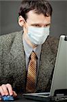 A man in a medical mask works with the laptop
