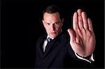 Businessman with his hand raised in signal to stop, isolated on black background, Studio shot
