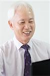old asian business man smiling and using a laptop